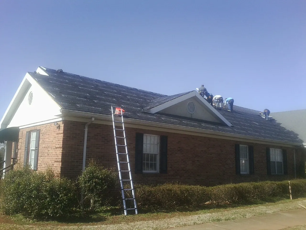 Crew tearing shingles off a brick ranch roof with a ladder set — Emergency Roof Repair work by our crew in Lewis Center