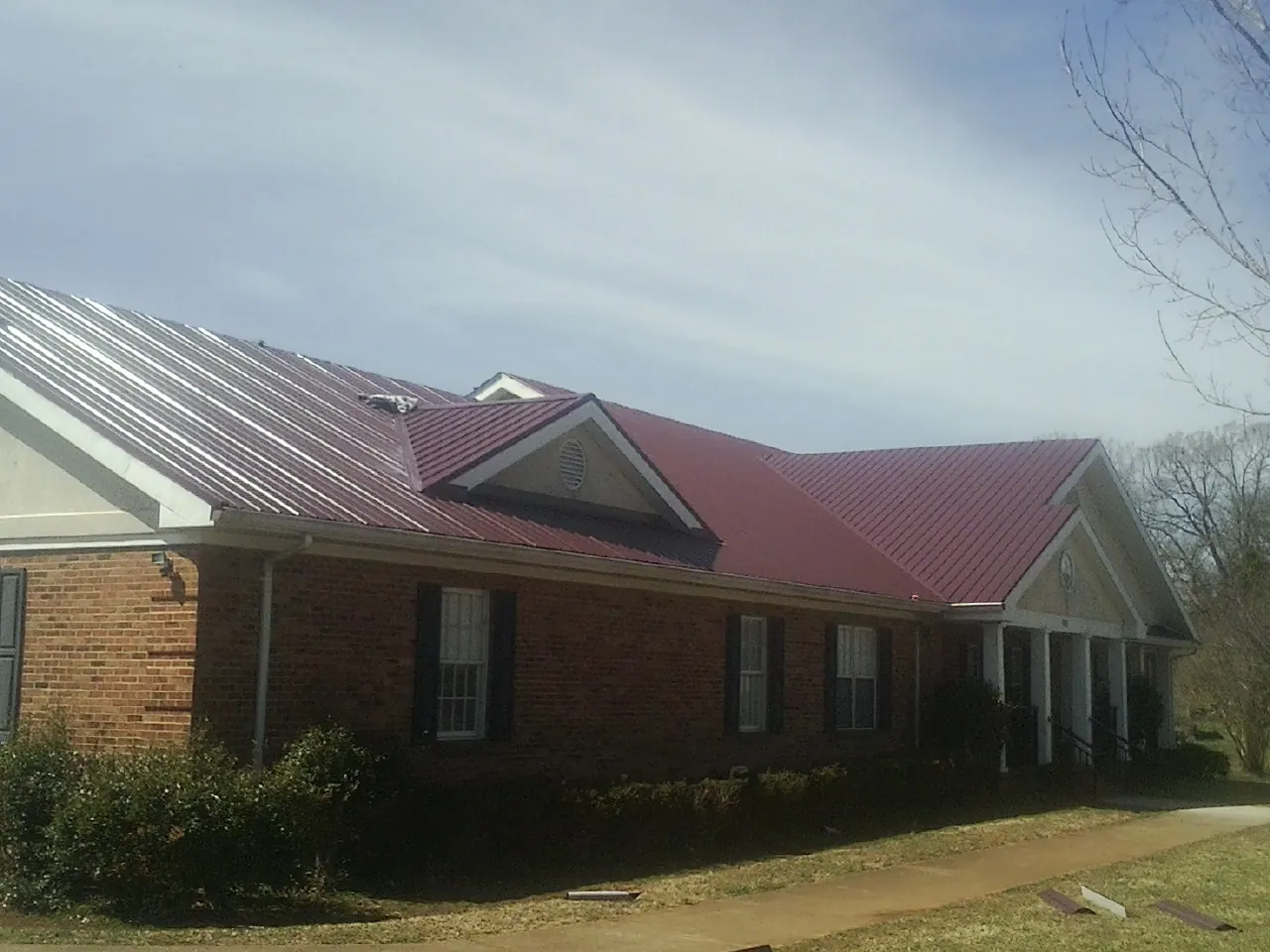 Red metal roof with gabled entries on a long brick building, from a Hail Damage Roof Repair job in Lewis Center