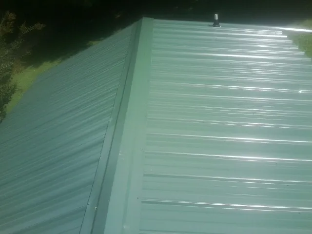 New green metal panels meeting at the ridge of a roof — Flat Roof Repair work by our crew in Lewis Center