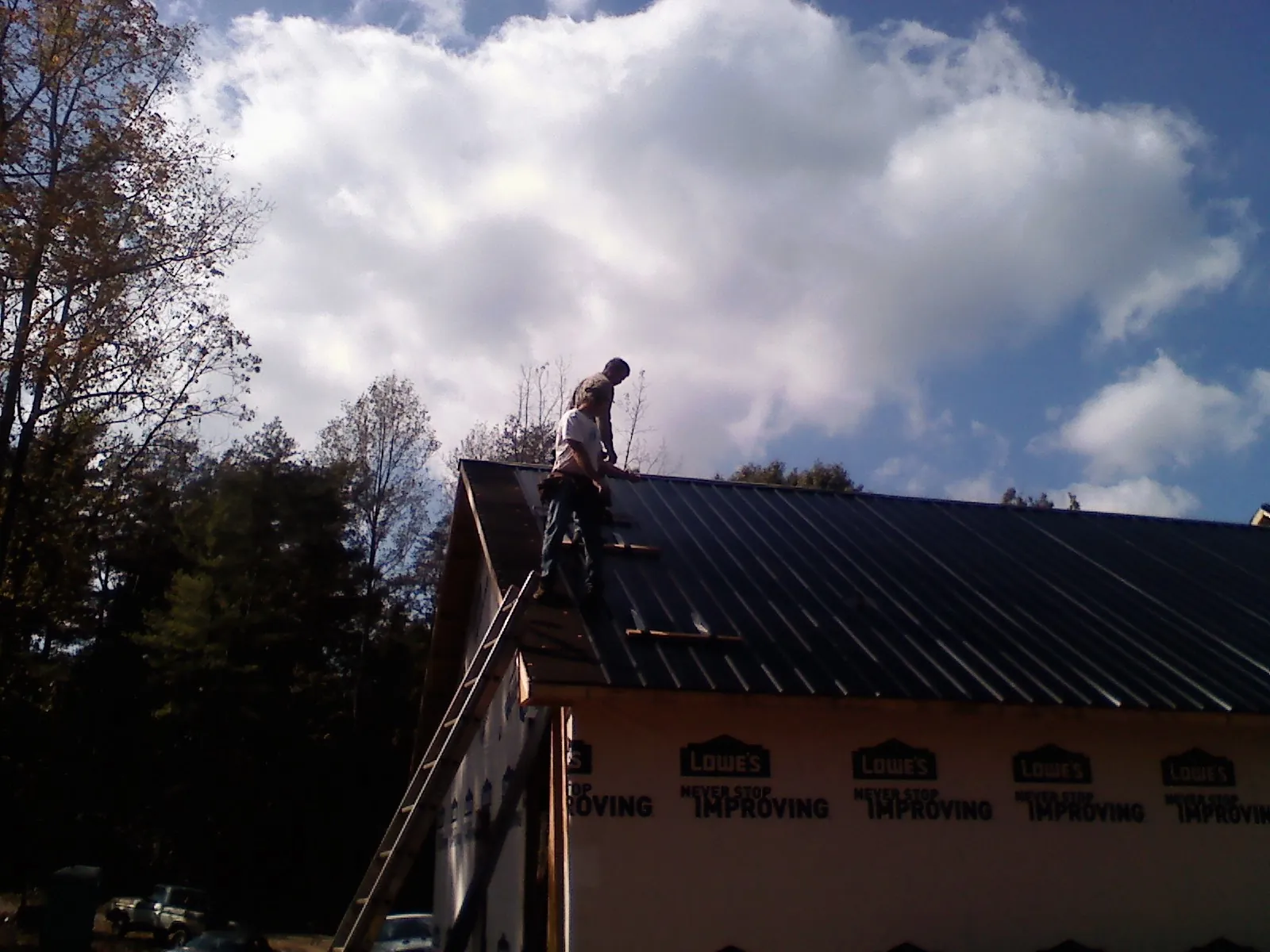 Roofer fastening dark metal panels high against a cloudy sky in Lewis Center