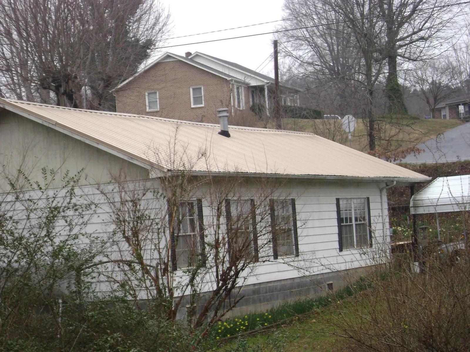 Tan metal roof on a white sided house set into a hillside — Commercial Roofing by Roofing Brothers in Lewis Center